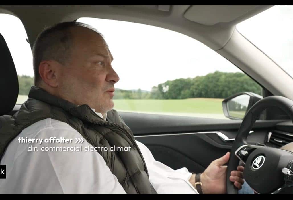 Thierry Affolter au volant d'une voiture, filmé de profil, la campagne défilant derrière la vitre, avec l'incrustation de l'émission Basik