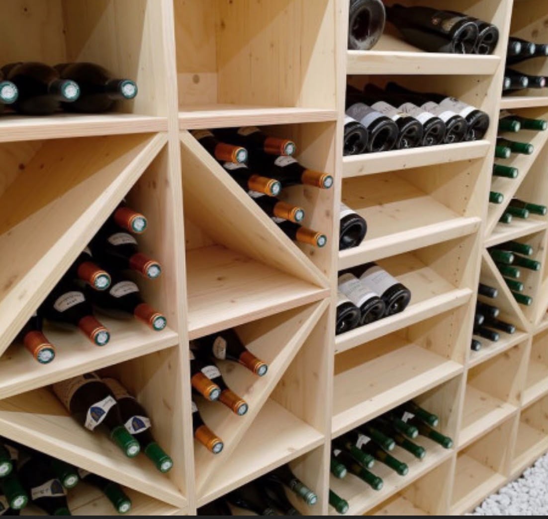 Casiers en bois clair en losanges et étagères droites accueillant des bouteilles couchées, sol en gravier blanc