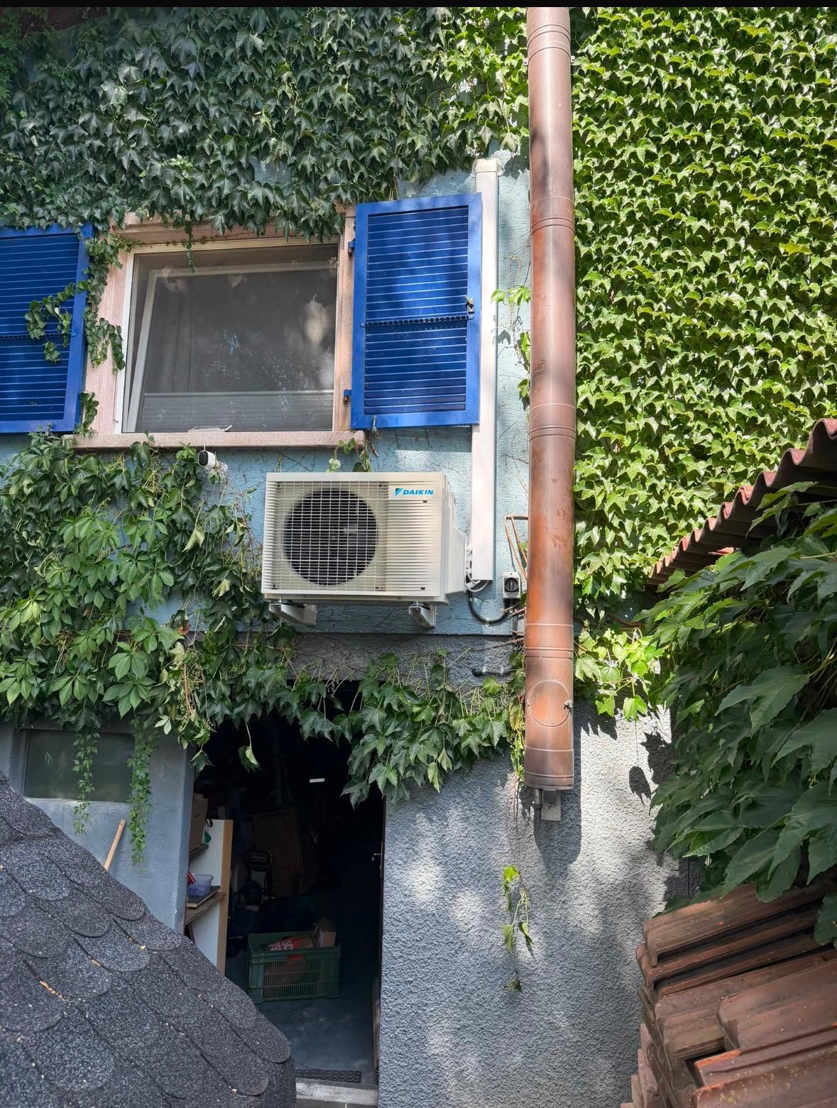 Unité extérieure Daikin fixée sur la façade d'une maison couverte de vigne vierge