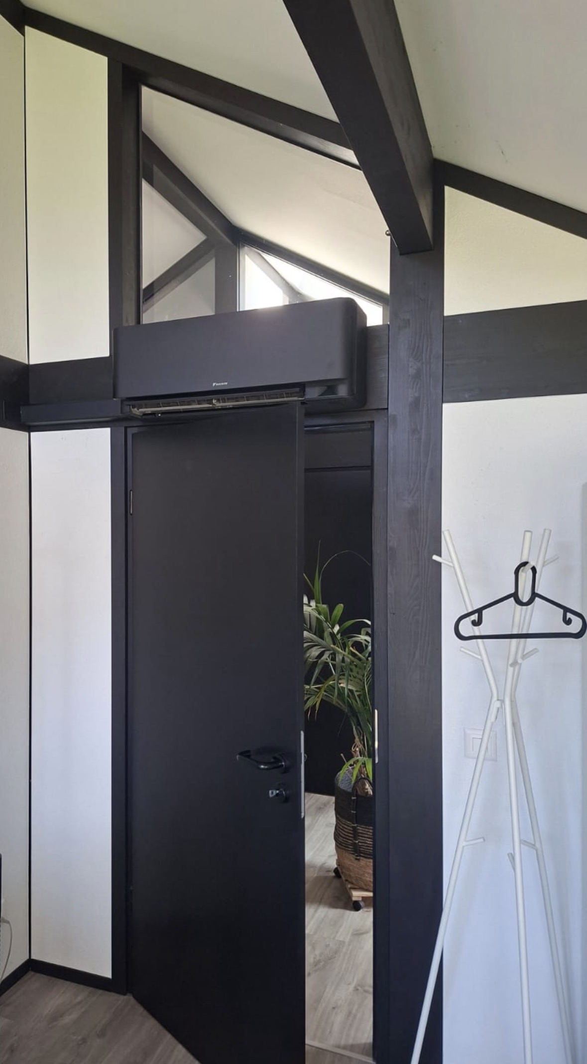 Unité murale Daikin noire installée au-dessus d'une porte, sous une charpente en bois sombre