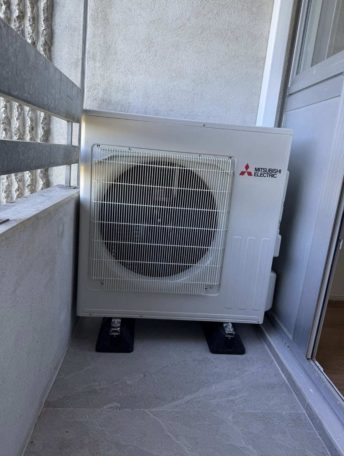 Unité extérieure de climatisation Mitsubishi Electric posée sur plots antivibratoires au sol d'un balcon