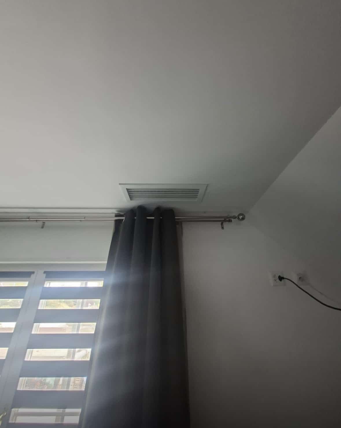 Grille de soufflage blanche encastrée au plafond d'une chambre, au-dessus d'une fenêtre