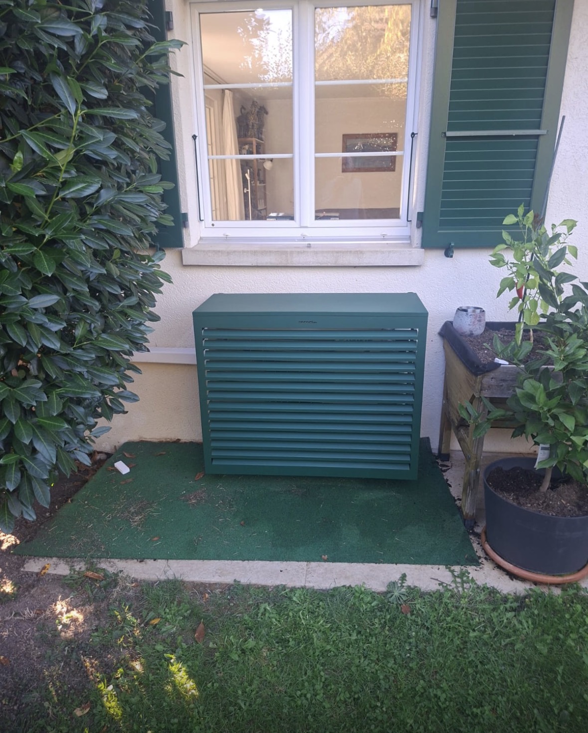 Cache de climatisation Decoclim vert à lames horizontales recouvrant l'unité extérieure, assorti aux volets de la villa
