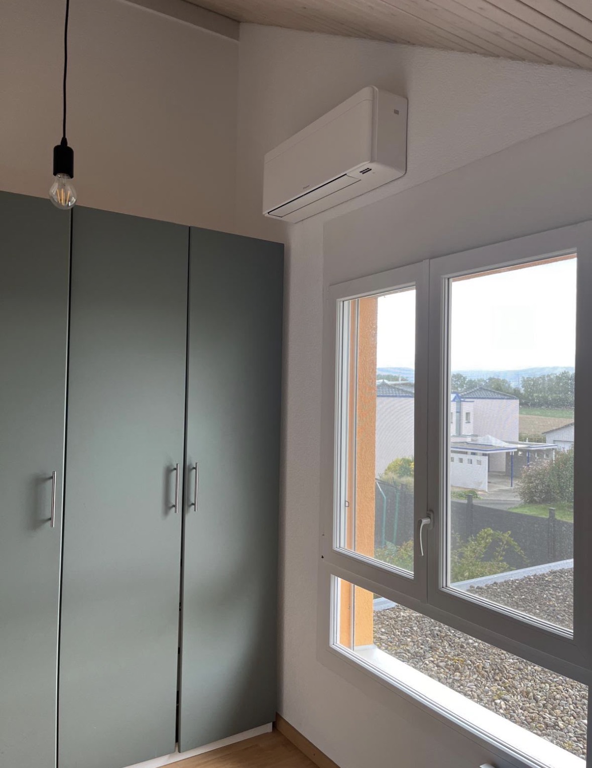 Split mural blanc installé dans une chambre au-dessus d'une fenêtre, à côté d'une armoire verte