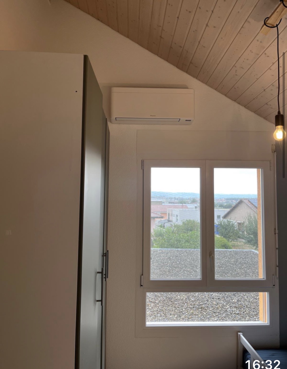 Unité intérieure Daikin sous une toiture en lambris clair, près d'une fenêtre avec vue dégagée
