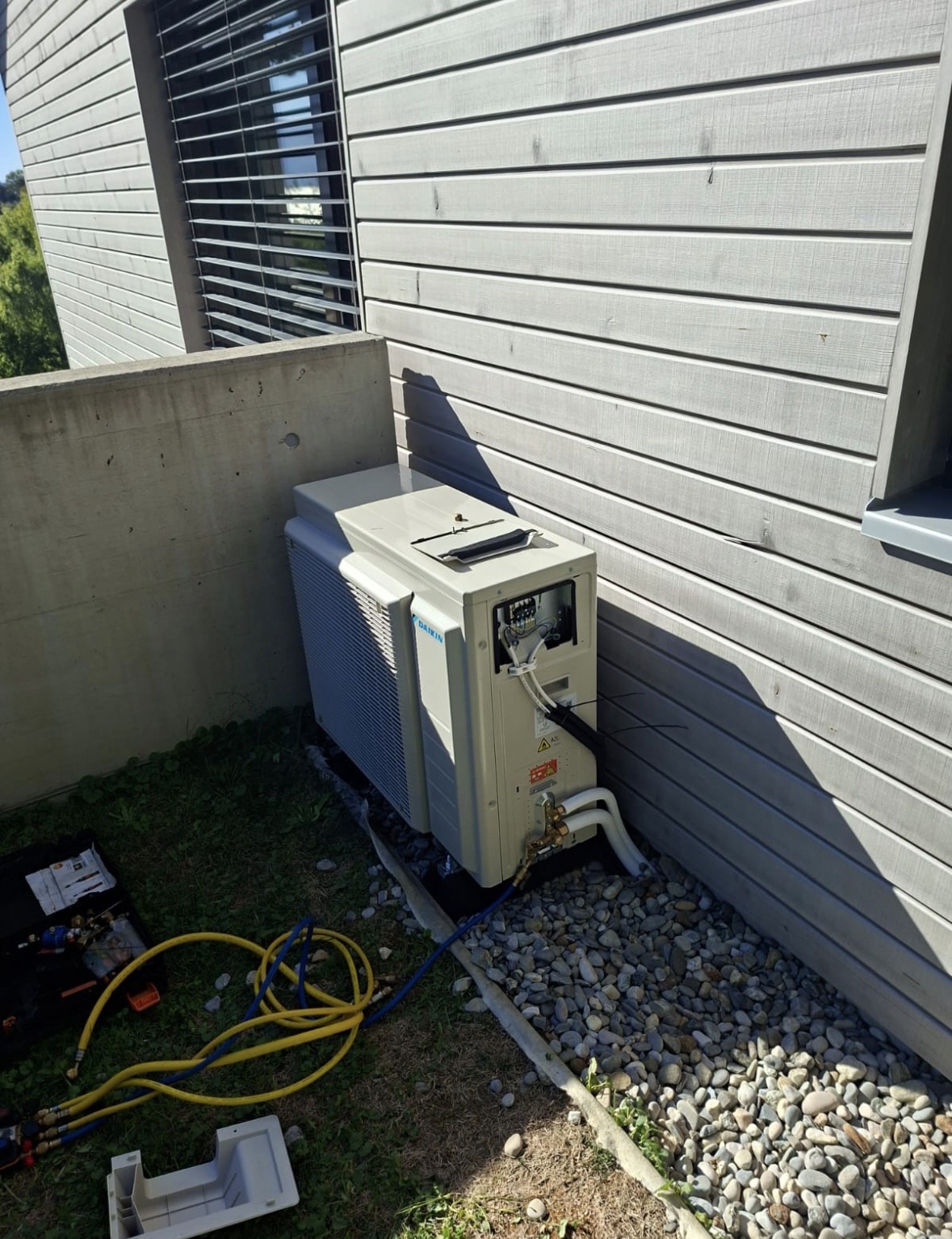Unité extérieure Daikin en cours de raccordement contre un bardage bois, outillage de mise en service au sol