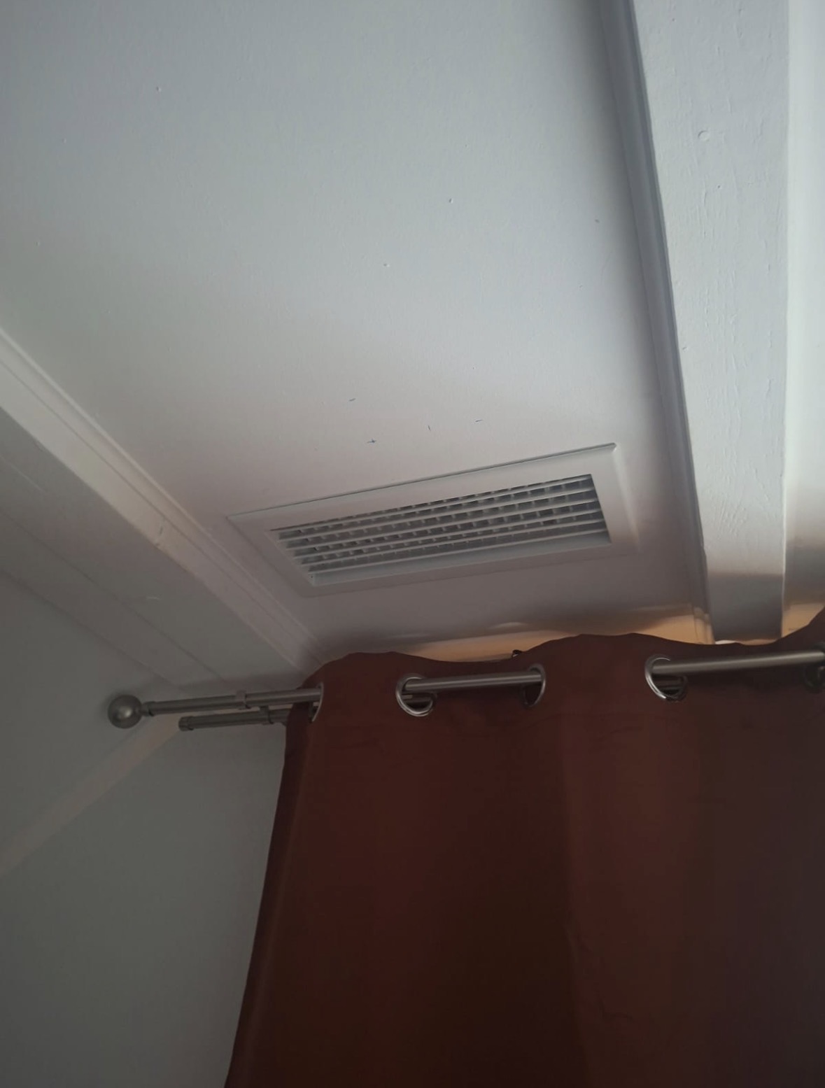 Grille de soufflage rectangulaire posée au plafond d'une chambre, près d'un rideau