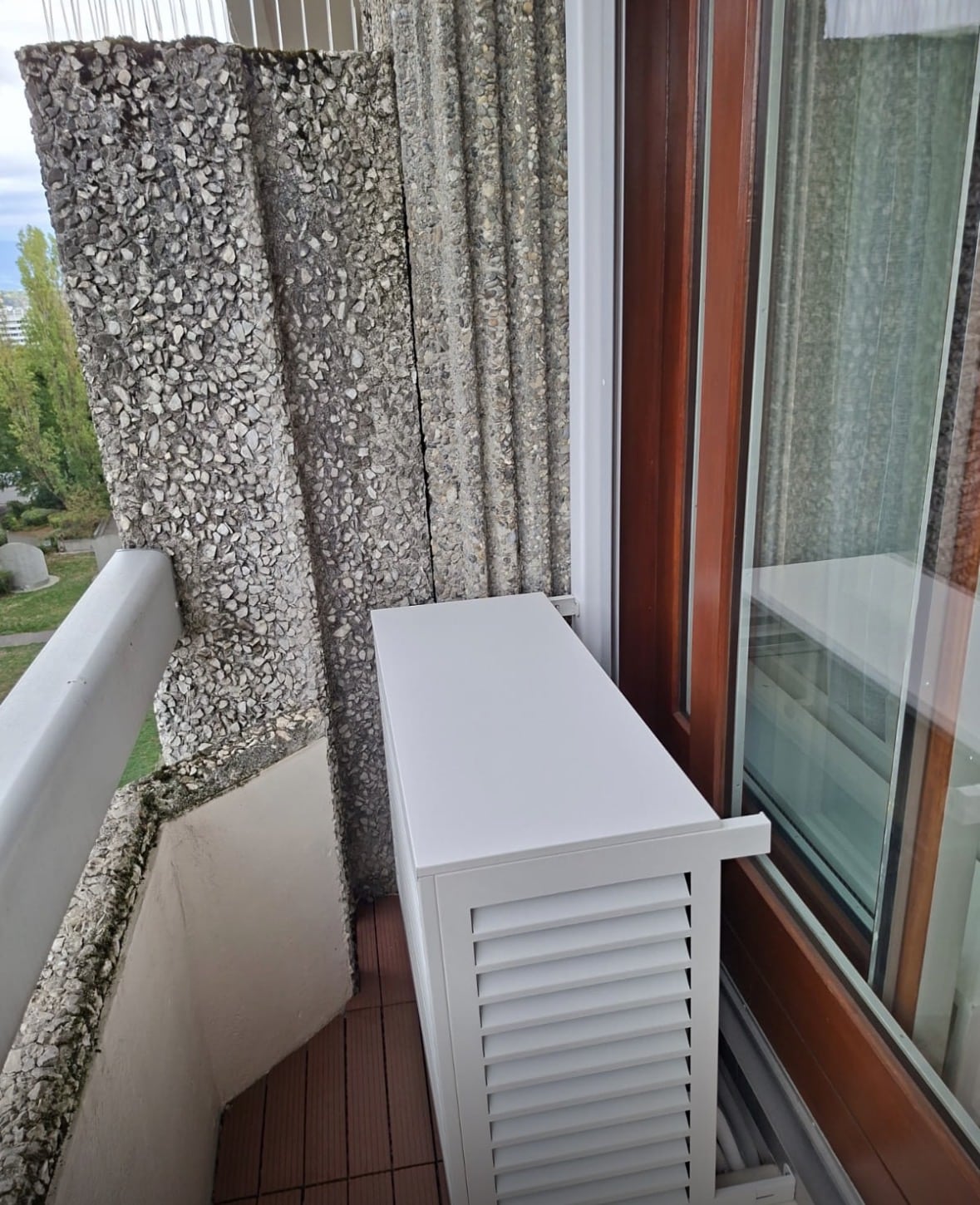 Cache-groupe Decoclim blanc à lames posé sur un balcon, le long d'une baie vitrée