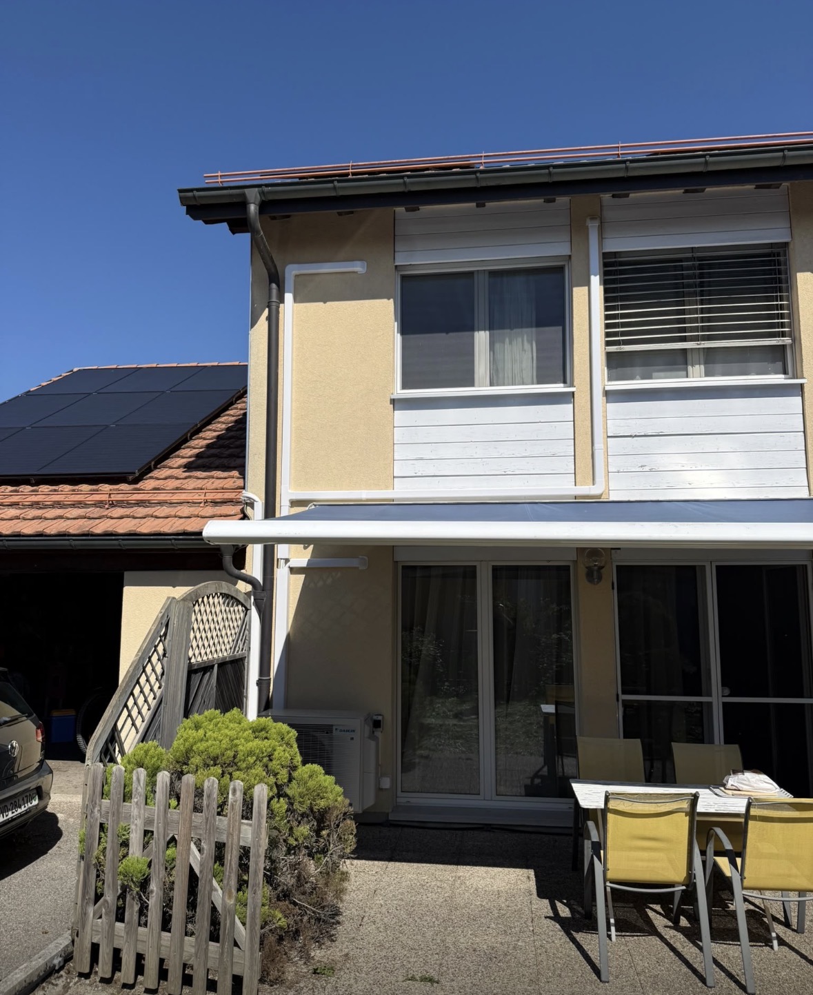 Façade de la villa avec la goulotte blanche et l'unité extérieure près de la terrasse