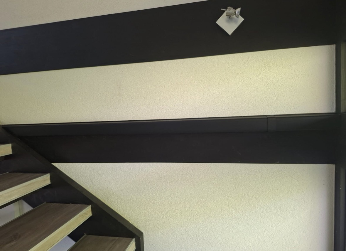 Goulotte noire intégrée dans le bandeau sombre le long de l'escalier intérieur