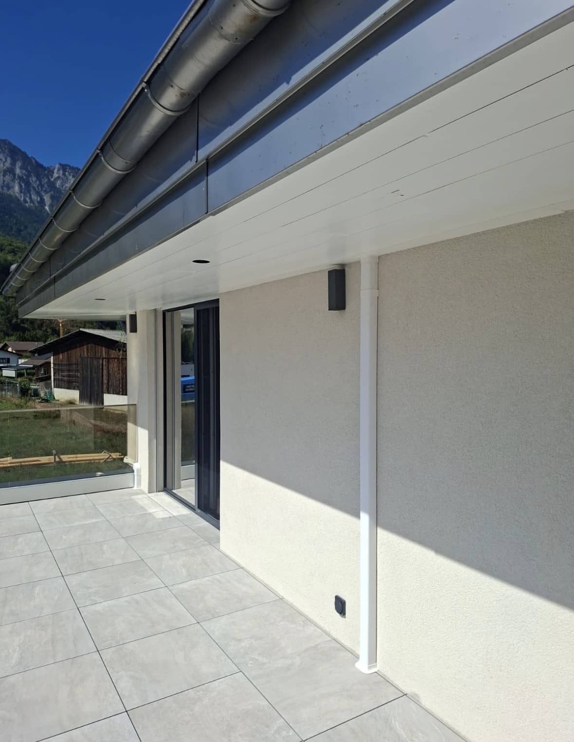 Façade et terrasse carrelée d'une villa neuve, sans goulotte apparente