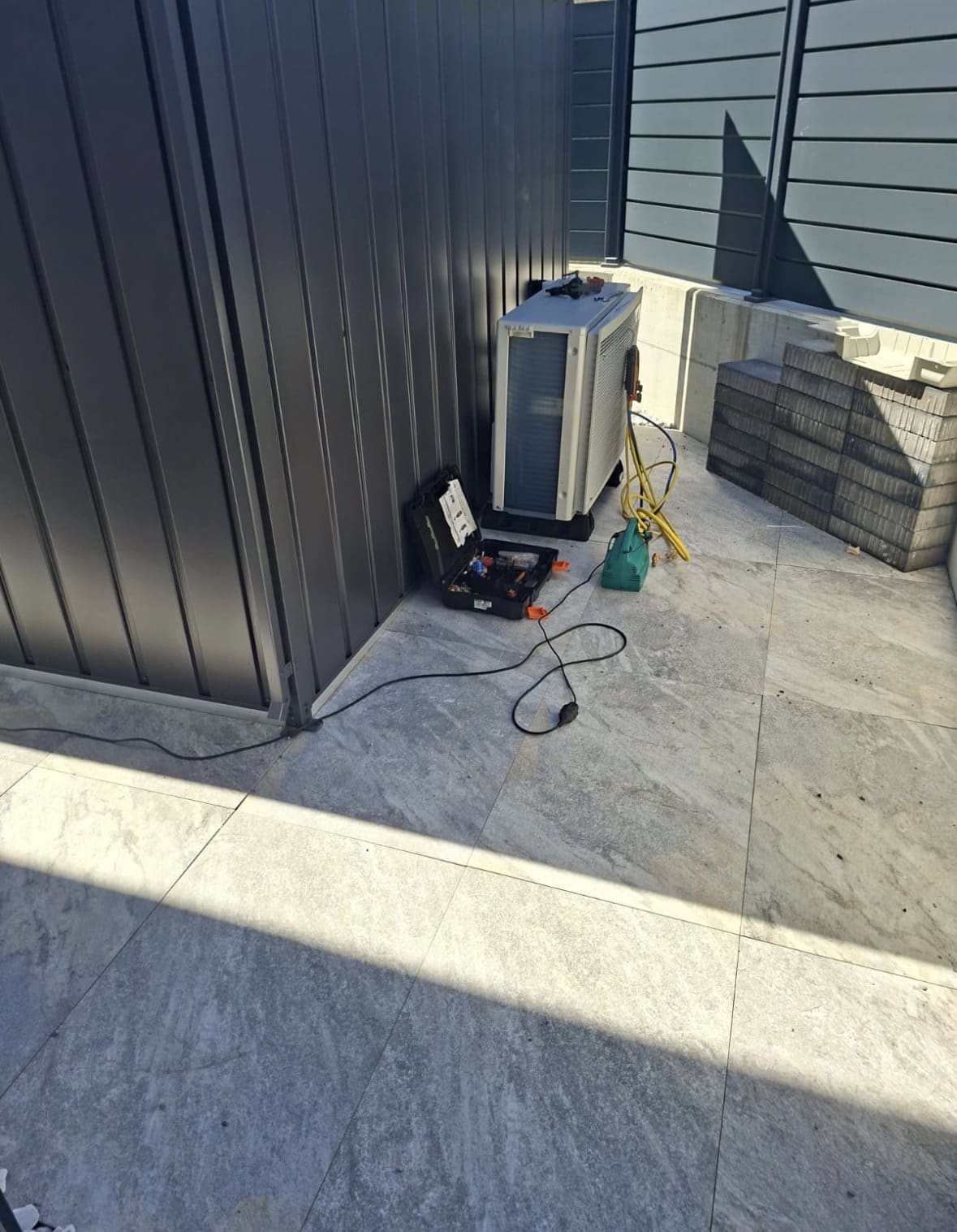 Unité extérieure de climatisation en cours de raccordement dans un angle de la terrasse