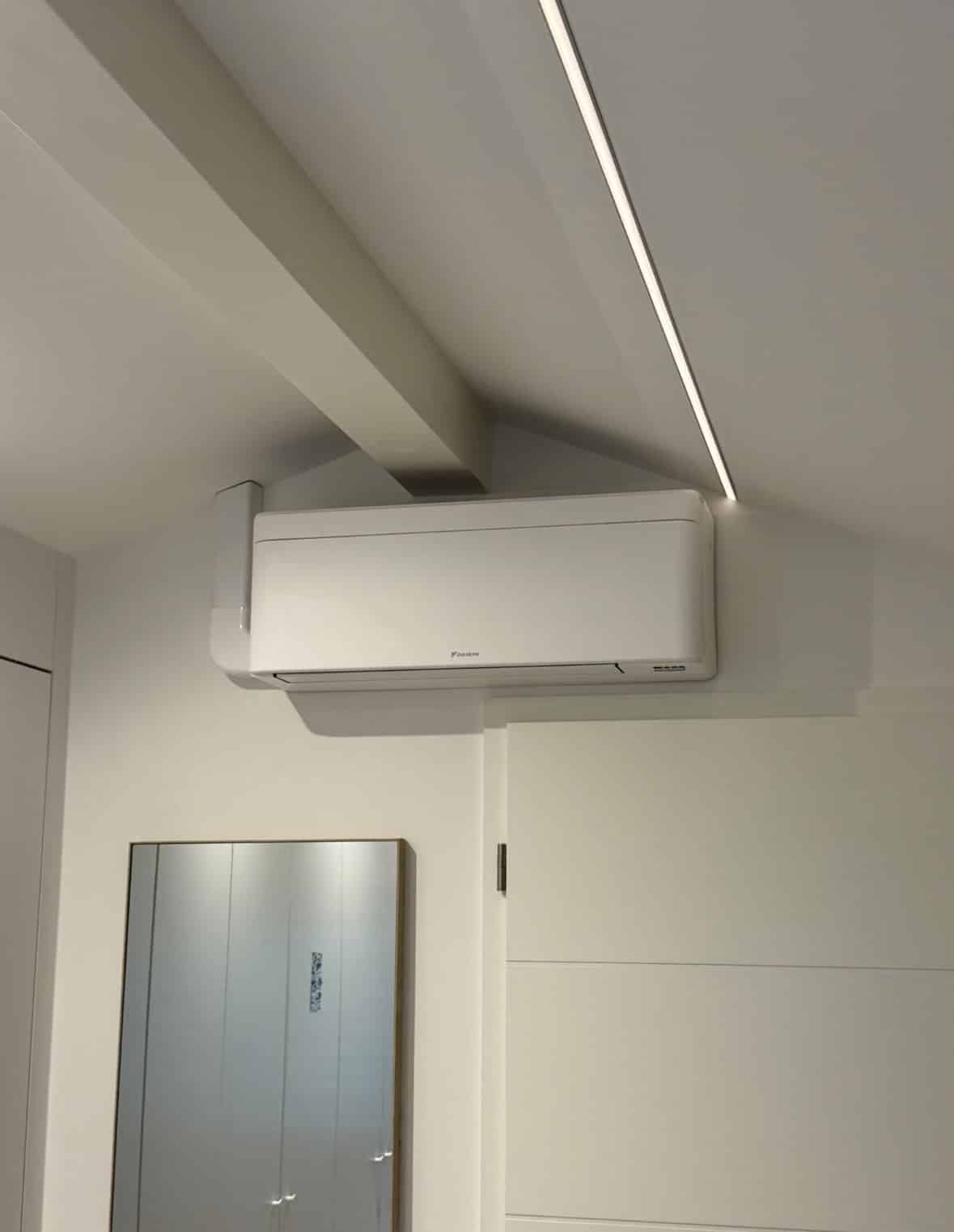 Unité murale Daikin blanche posée en hauteur sous un plafond mansardé, près d'une ligne lumineuse