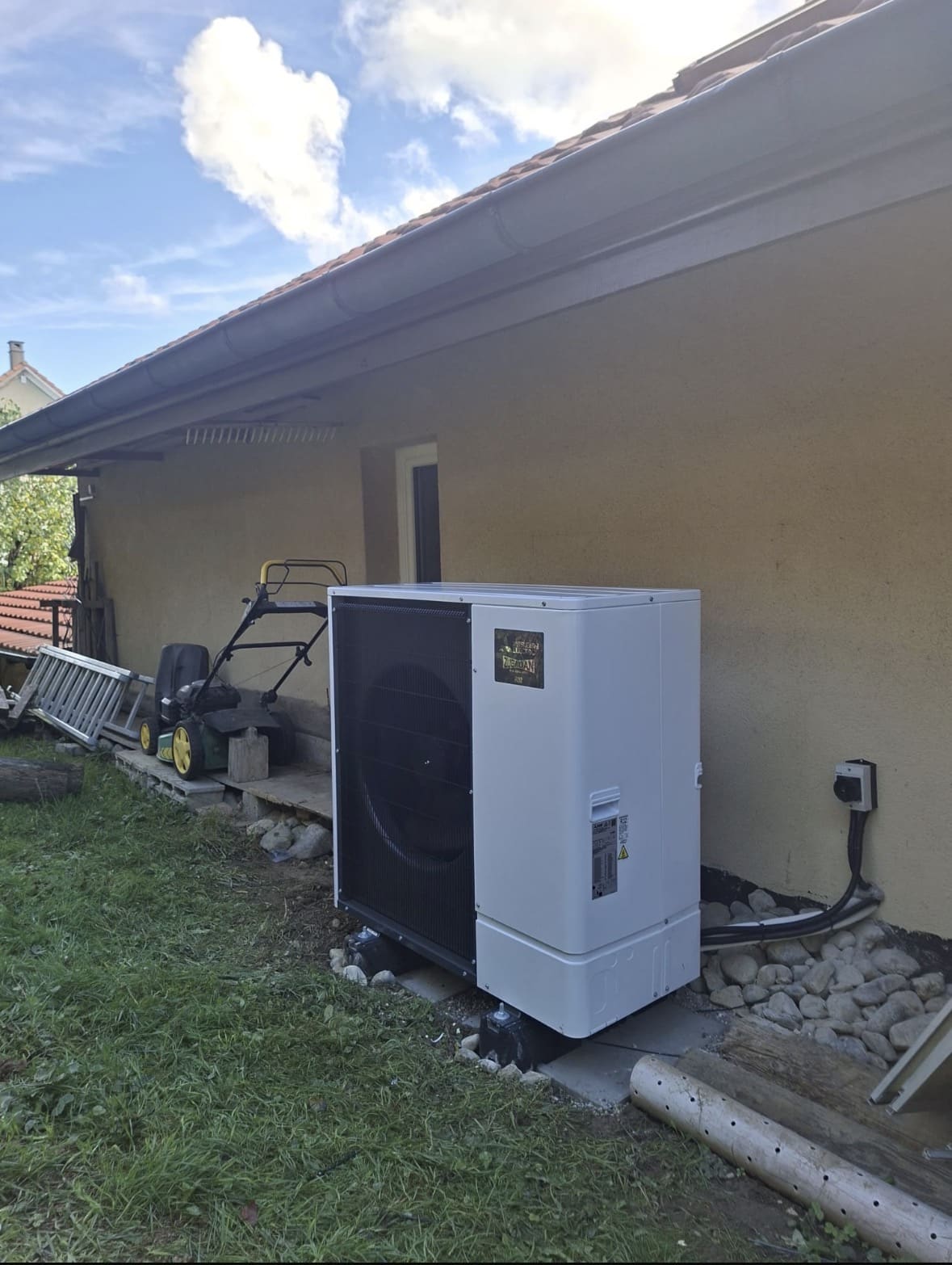 Unité extérieure de pompe à chaleur air-eau Mitsubishi installée sur plots le long de la façade d'une villa