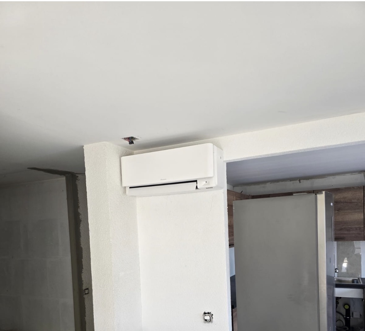 Unité intérieure murale Daikin blanche posée en partie haute d'un mur, au-dessus du passage vers la cuisine d'un appartement