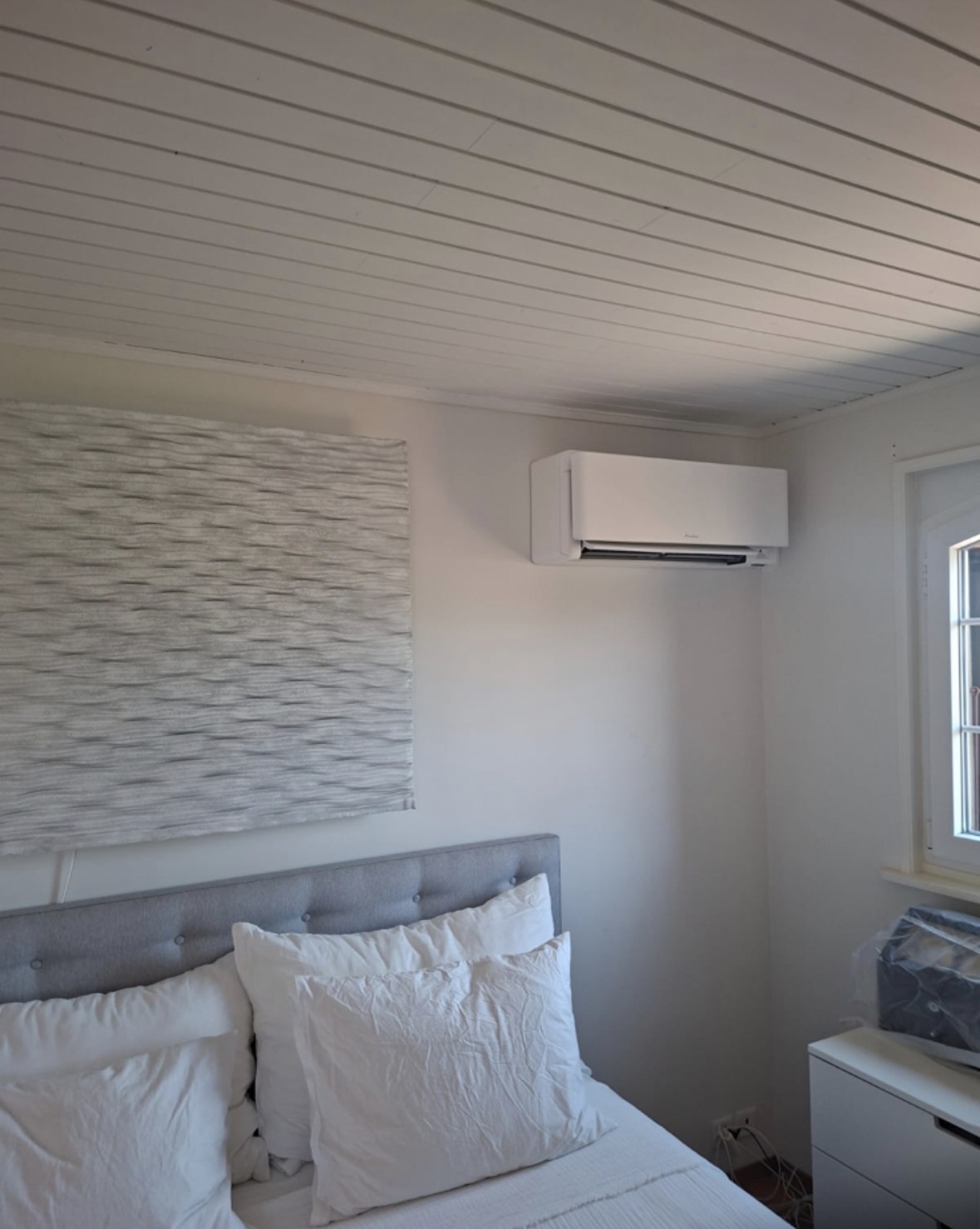 Unité murale de climatisation Daikin blanche installée en hauteur dans une chambre aux murs clairs