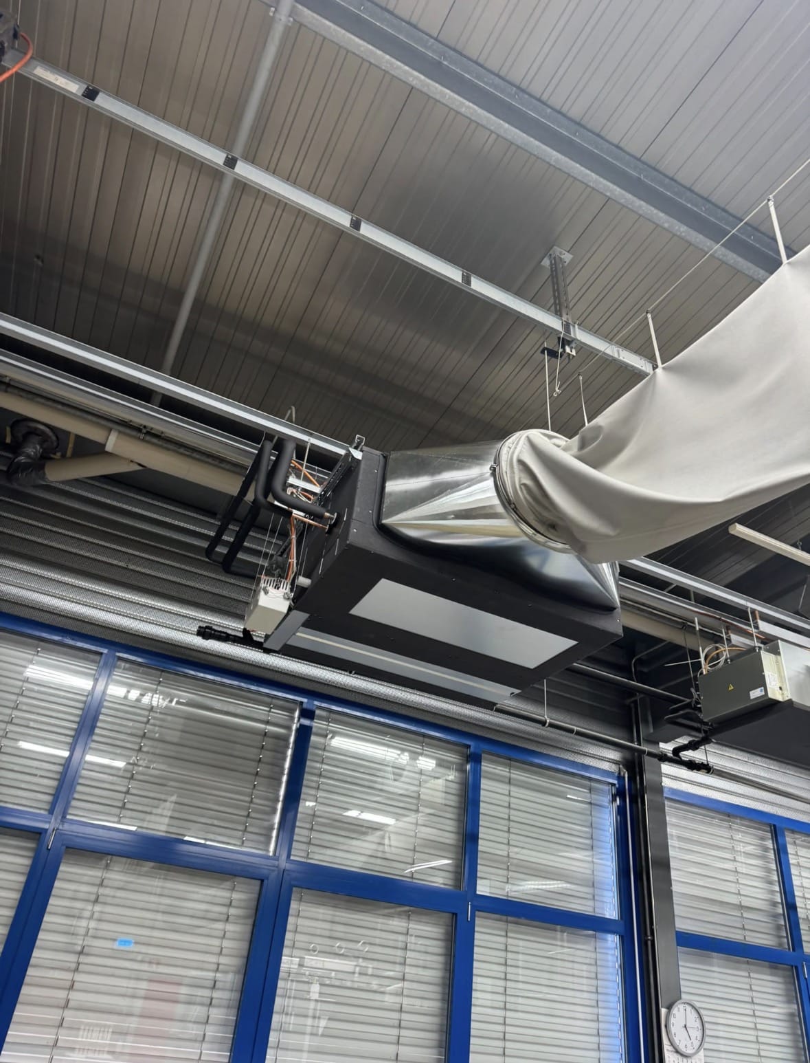 Unité gainable suspendue sous la charpente de l'atelier, raccordée à une gaine textile de diffusion