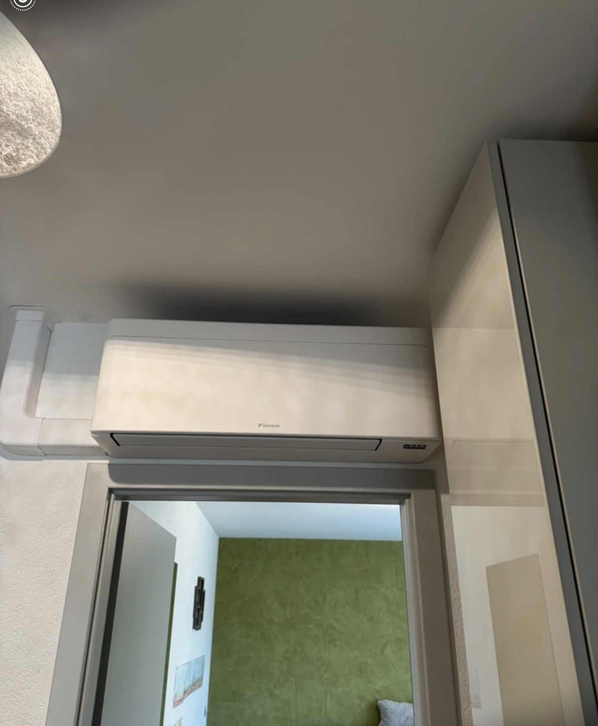 Split mural Daikin et goulotte blanche longeant le plafond près d'une armoire