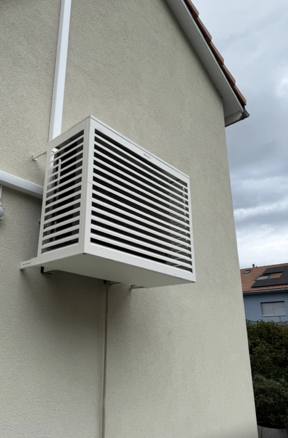 Vue rapprochée du cache Decoclim blanc à lames horizontales protégeant la pompe à chaleur air-air en pignon de villa