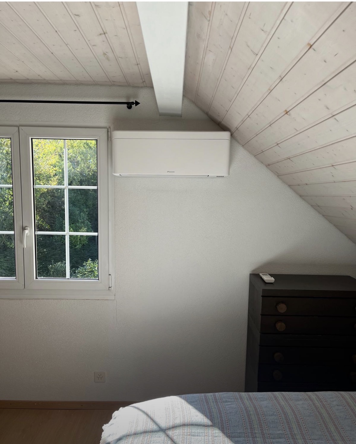 Split mural Daikin installé dans une chambre sous combles au plafond en bois clair