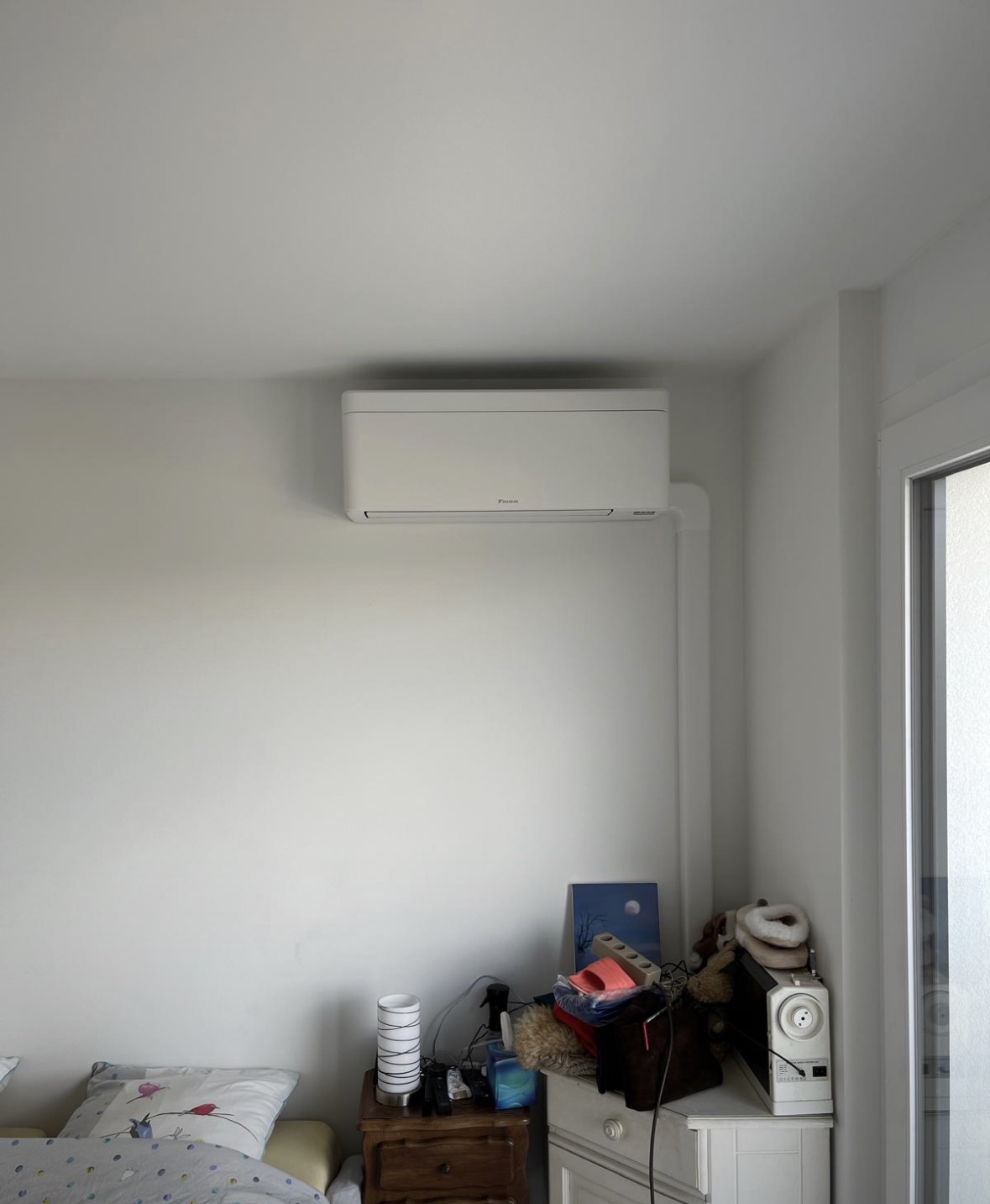 Split mural Daikin installé dans une chambre, avec goulotte blanche descendant vers la baie vitrée
