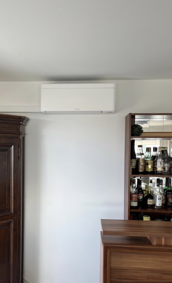 Unité intérieure murale Daikin blanche installée en haut d'un mur clair dans un séjour avec mobilier en bois
