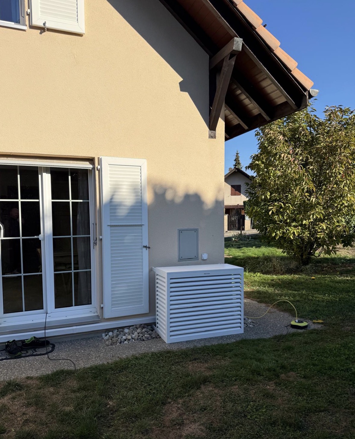 Unité extérieure de climatisation protégée par un coffrage blanc à lamelles le long de la façade d'une villa