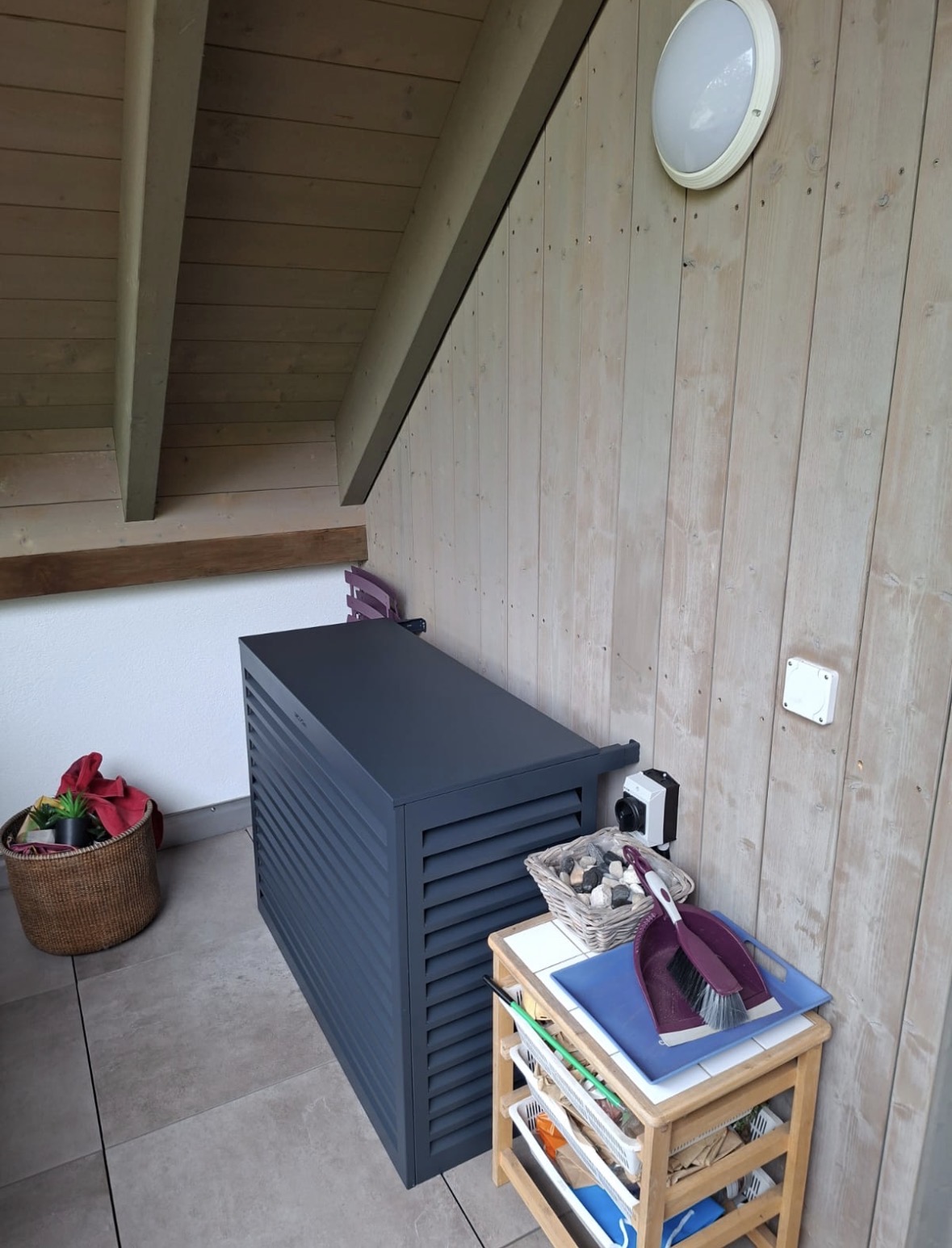 Groupe extérieur habillé d'un cache anthracite à lamelles, installé sur un balcon en bois