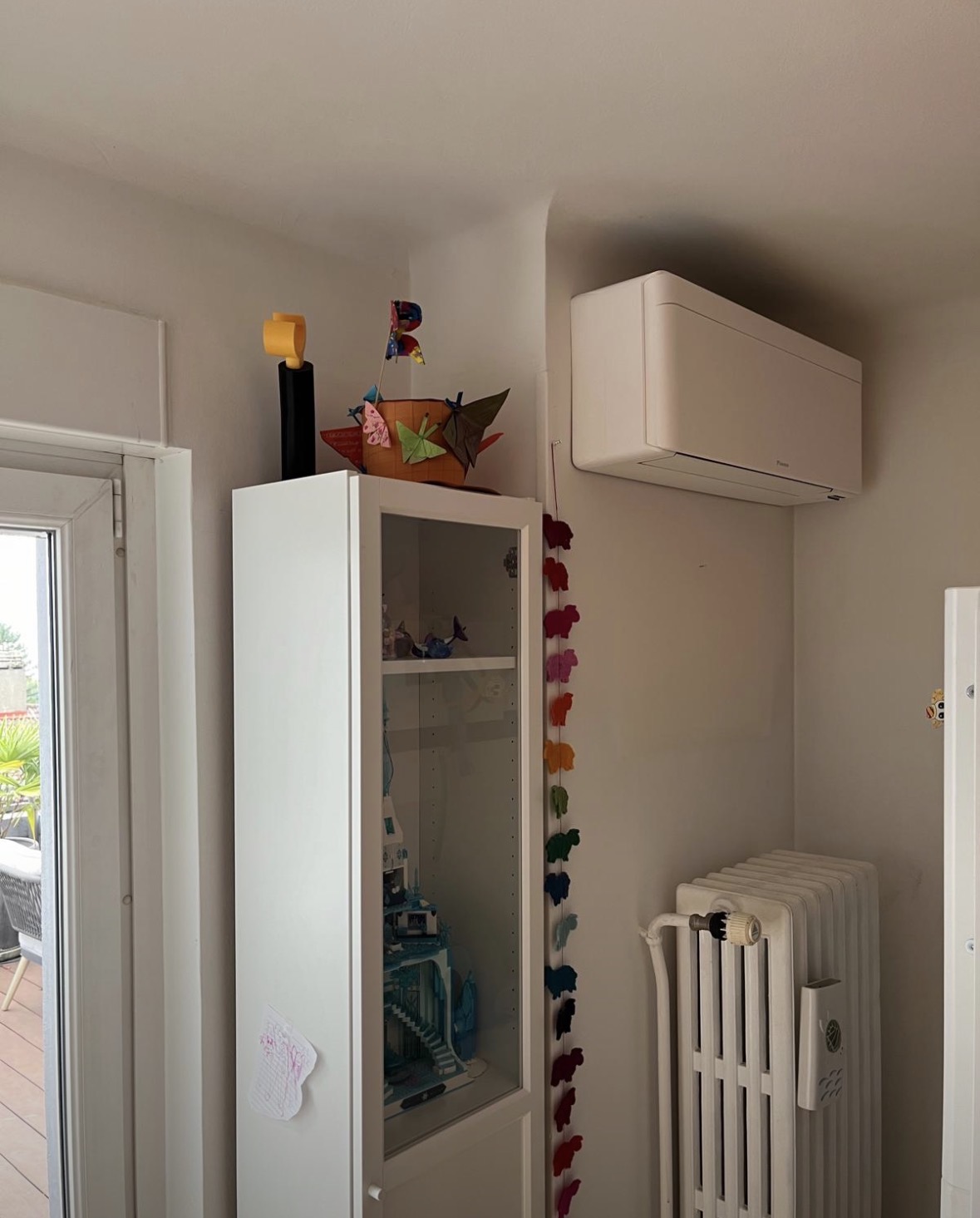 Unité intérieure Daikin Stylish placée dans un angle de pièce, au-dessus d'un radiateur existant