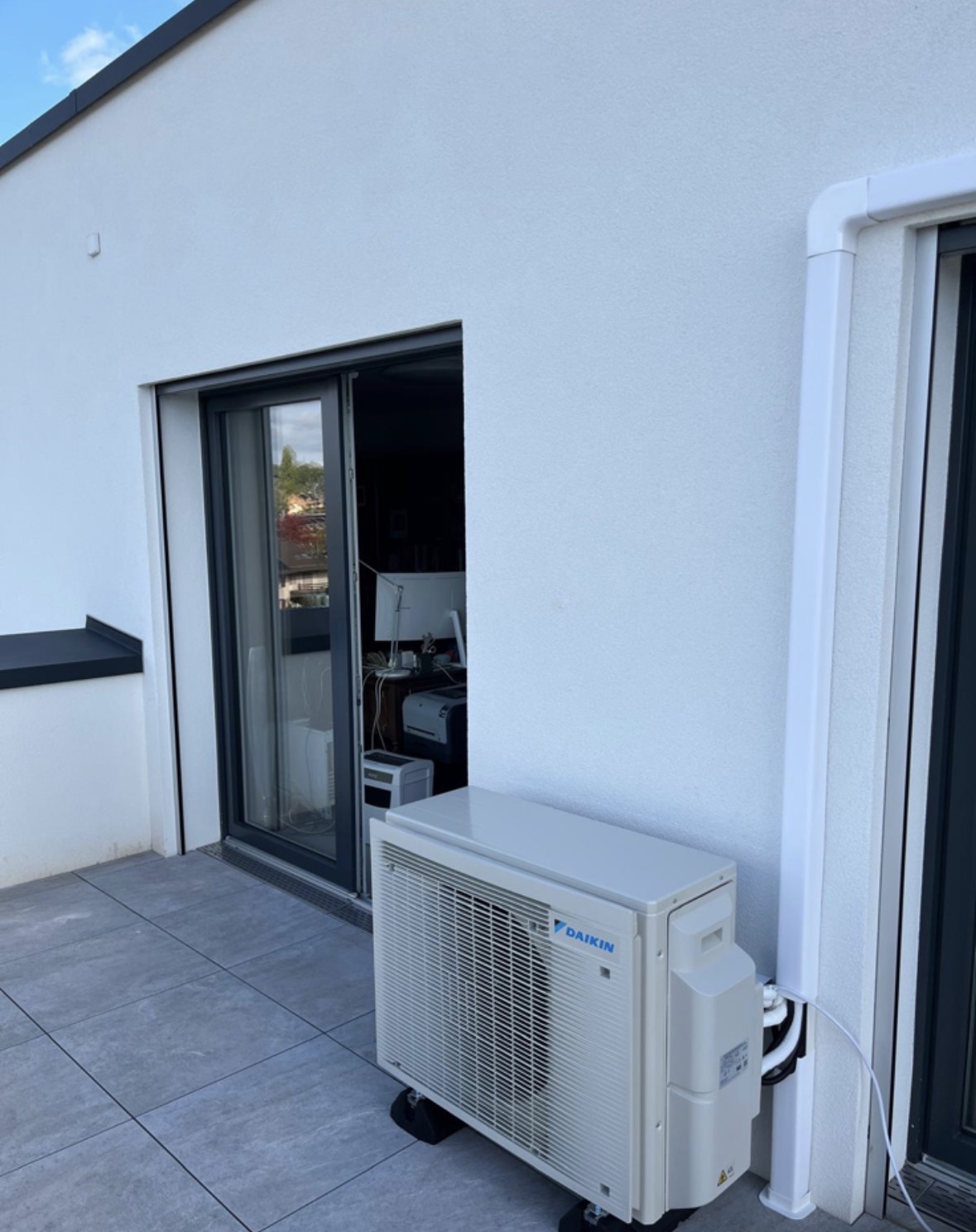 Unité extérieure Daikin installée sur la terrasse d'un appartement en attique, le long de la façade blanche
