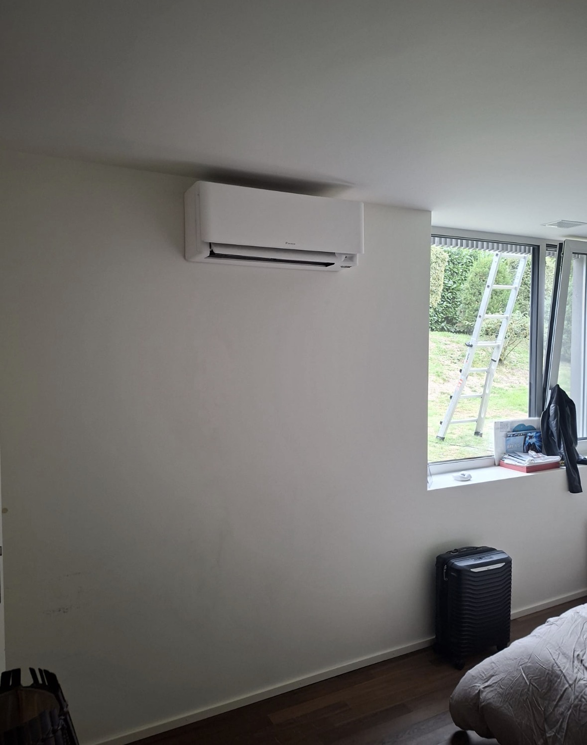 Split mural Daikin blanc installé dans une chambre aux murs clairs, près d'une baie vitrée